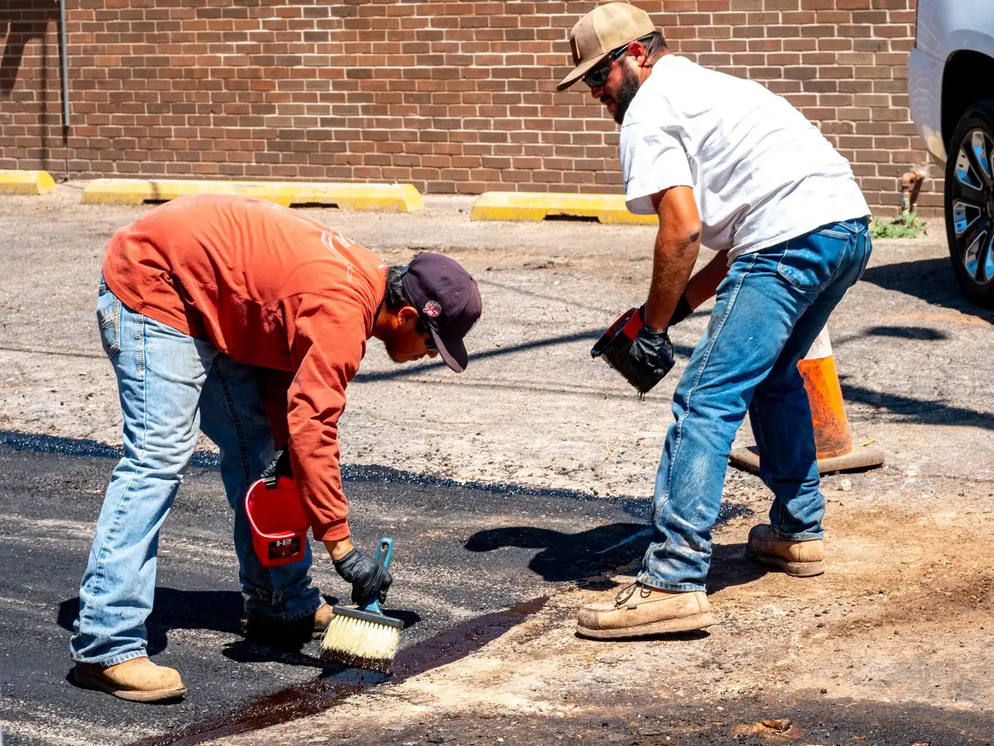 Two workers brushing sealant over an asphalt repair in a parking lot