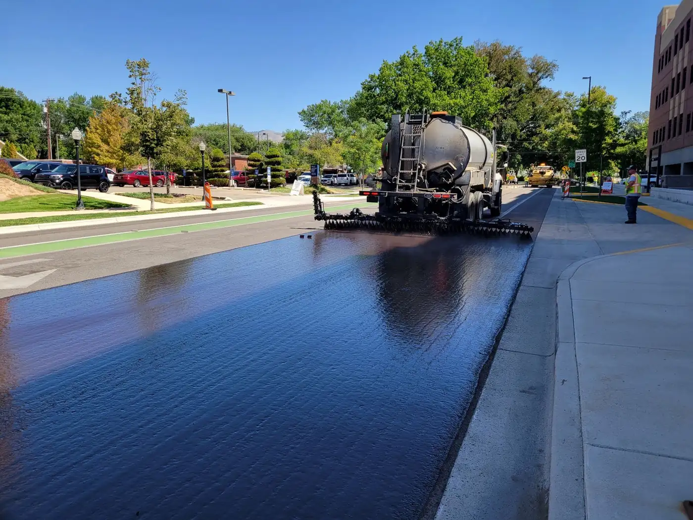 Distributor truck spraying a glossy black seal coat across an asphalt street